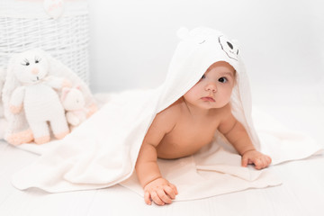 Cute baby under a white towel with a hood after a bath. Baby in a towel. Children's portrait. Healthcare concept.