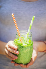 Summer healthy detox drink: blended green smoothie in the bright midday sun, in the hands of a young girl, selective focus.