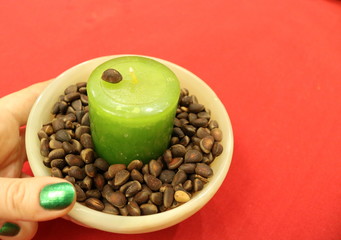 Pine nuts around a green candle in a stone Cup held by a woman's hand on a red cloth background.  