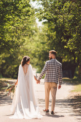 Happy bride and groom holding hands and walking in garden wedding day. Back view of charming stylish newlyweds holding hands while walking in park forest. Path to future life. happy marriage moments