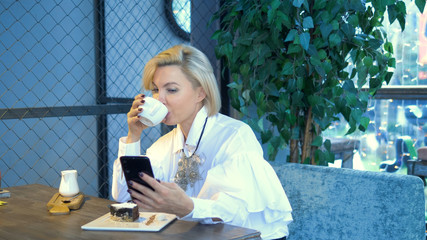 elegant stylish blond woman using mobile phone sitting in a cafe