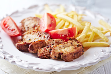 Fried pork tenderloin with tomatoas and french fries. Bright backgroun