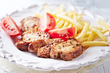 Fried pork tenderloin with tomatoas and french fries. Bright background