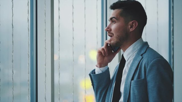 Business man is standing near the window. Man is lon phone. He is isolated, on white blurred background. Copy space. 4K.