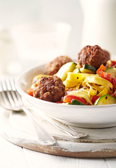 Tagliatelle pasta with meatballs, red pepper and zucchini. Bright background.