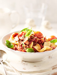 Pappardelle Pasta with cherry tomatoes, red onion and fresh basil on white wooden background.