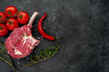raw beef steak, beef tomahawk with spices, tomatoes, thyme on a stone background. with copy space...