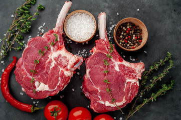 two raw steaks, beef tomahawk with spices and thyme on a stone background.