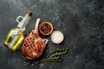 steak - grilled beef tomahawk with spices, sunflower oil, thyme on a stone background.