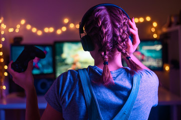 Gaming and e-sports. A streamer girl plays games using the joystick and gamepad. On three monitors, creative light