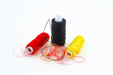 Coils with black, red and yellow threads of different colors close-up on a white background. A needle is inserted into a spool of black thread
