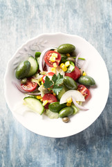 Healthy salad with green olives, sweet corn, cherry tomatoes, red onion, baby spinach, capers and fresh herbs. Bright wooden background. Top view. 