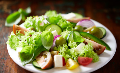 Healthy salad wwith feta cheese, green olives, cucumber, red onion, green pepper, various tomatoes and fresh basil. Close up.