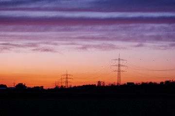 Naklejka premium Beautiful dramatic orange and blue cloud and sky after storm and raining over agricultural field and high voltage tower on countryside in Germany. Nimbostratus cloud during sunset. 