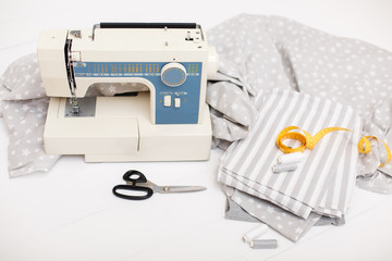 process of sewing of bed linen on sewing machine. Sewing kit. Grey fabric, scissors, threads, measuring tape and sewing machine on white wooden background