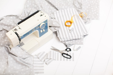 Fototapeta na wymiar process of sewing of bed linen on sewing machine. Sewing kit. Grey fabric, scissors, threads, measuring tape and sewing machine on white wooden background