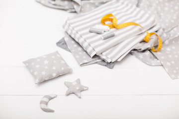 process of sewing of bed linen and little cute decorative pillow, star and moon. Sewing kit. Grey fabric, threads, measuring tape and sewed objects on white wooden background