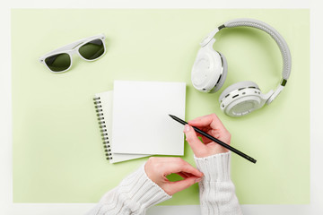 Top view mock up woman's hands with notebook, headphones, glasses on green background. Copy space. 'To do' list. Planning of winter walk route, to-do list or shopping. Relax, wish list, play list