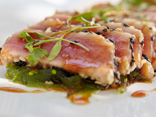 Seared ahi tuna slices on a bed of seaweed salad sprinkled with sesame seeds and oil and garnished with sprouts