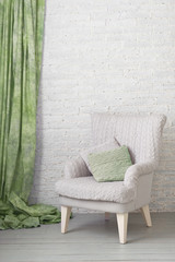 soft armchair near white brick wall with green curtain. Arm-chair with knit upholstery