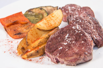 A beef sirloin with baked potatoes and some vegetables dish