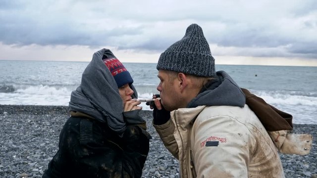 homeless couple, man and woman smoking on the seashore