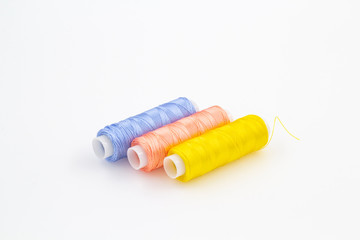 Spools of yellow pink and blue threads on a white background
