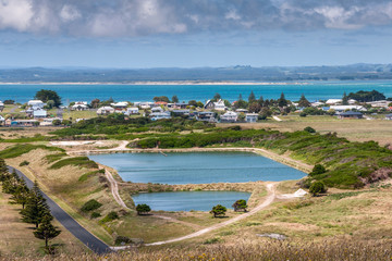 Stanley, Tasmania, Australia - December 15, 2009: Fresh water reservoir slightly above the white houses of the town with ocean in back. Mountains under cloudscape on horizon.