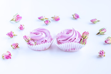 Pink fruit marshmallows and dried buds of roses on the white background. 