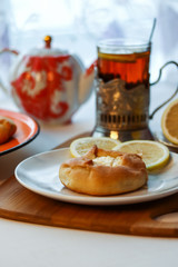 Cosy breakfast concept, transparent cup of tea with lemon and pastry on white background, near the window, front view, closeup, vertical