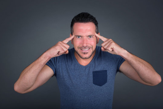 Young handsome caucasian man concentrating hard on an idea, with a serious look, thinking with both index fingers pointing to forehead eyes closed.