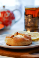 Cosy breakfast concept, transparent cup of tea with lemon and pastry on white background, near the window, front view, closeup, vertical