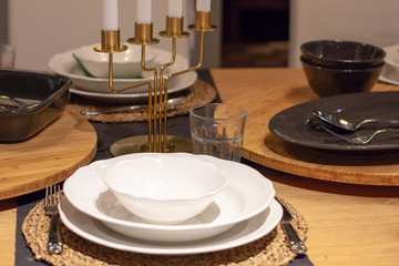 Festive table setting served with whiten plates, bamboo stands and gold candlestick for four candles in the middle. Horizontal orientation.