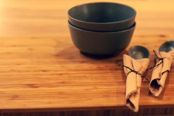 Wooden board with a stack of two empty clay bowls and two spoons, beautifully folded brown napkins. One spoon is partly visible.