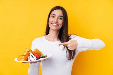 Young brunette woman holding waffles over isolated background and pointing it