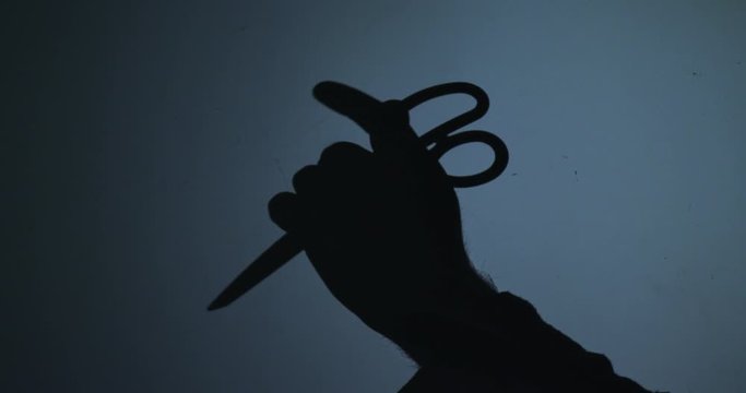 Silhouette of hands with a pair of scissors on a blue background