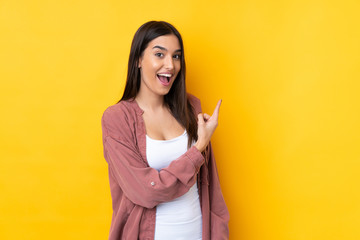 Young brunette woman over isolated yellow background surprised and pointing side
