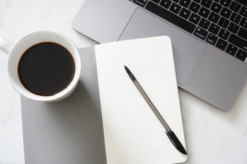 An open notebook and pen ready to write a to do list with a cup of coffee and laptop on a desk; minimal clean gray and white; flat lay