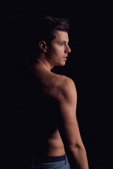 barechested guy with a dramatic light in the Studio on a black background. looking in the direction of the light