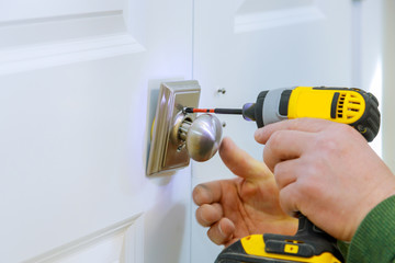 Handyman using a drill to installing lock in door in a house
