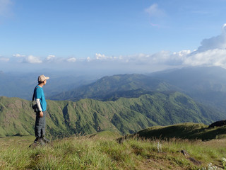  A young Asian man stands on a large rock in the winter mountains enjoying the natural