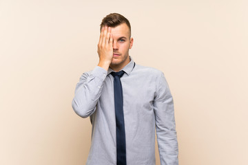 Young blonde businessman over isolated background covering a eye by hand
