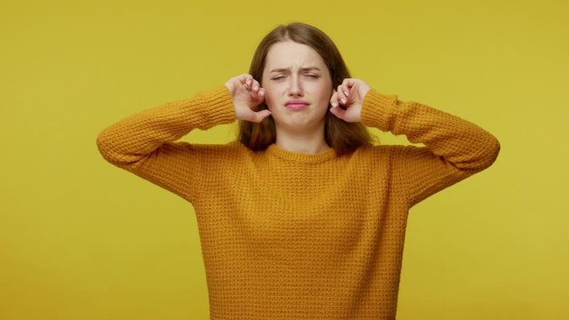 Don't want to listen. Upset girl in casual clothes covering ear with arms and saying no, not hearing talk, ignoring loud noise, avoiding annoying sound. studio shot isolated on yellow background