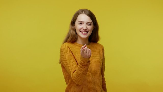 Come here to me! Smiling positive attractive girl with kind face expression showing beckoning gesture, inviting to meet, looking playful flirtatious. indoor studio shot isolated on yellow background