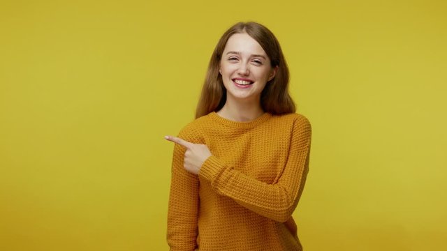 Smiling happy beautiful girl with kind face expression in pullover pointing to side empty place on yellow background, copy space for idea presentation, advertising area. indoor studio shot, isolated