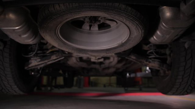 Close-up of underbody while car lifting during vehicle maintenance in auto repair service. Automobile mechanic raising car with special lift to check chassis during technical inspection in garage