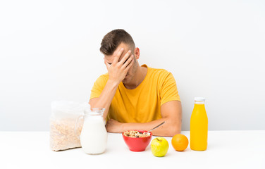 Young blonde man having breakfast covering eyes by hands