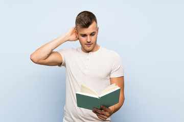 Young handsome blonde man over isolated blue background holding and reading a book