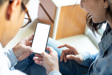 Mockup image blank white screen cell phone.couple hand holding texting using mobile on sofa at home.background empty space for advertise text.people contact marketing business and technology