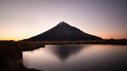 Fototapeta premium Majestic Mount Taranaki reflected in the clear water of Pouakai tarn at dawn